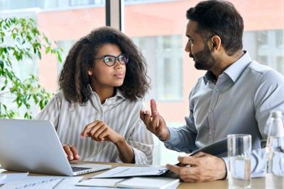 IT support mentor explaining information to female colleague on laptop. 